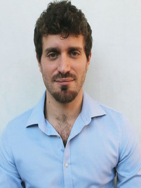 DR with short brown hair and facial hair.  Wearing a light blue open neck shirt against a light background.